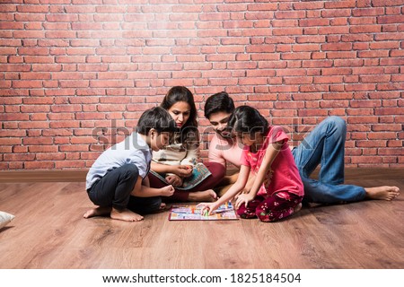 Indian young family of four playing board games like Chess, Ludo or Snack and Ladder at home in quarantine