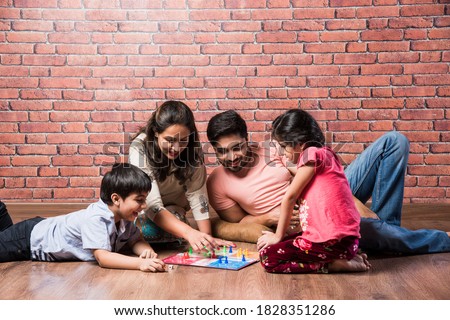 Indian young family of four playing board games like Chess, Ludo or Snack and Ladder at home in quarantine