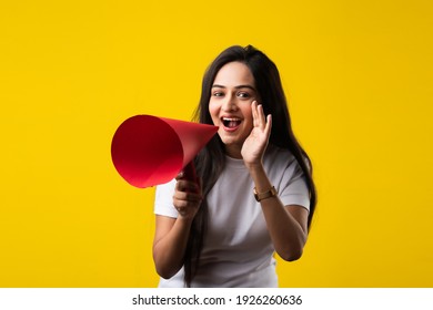 Indian young girl with megaphone made out of paper. Announcing, screeming or advertising while standing against yellow studio background