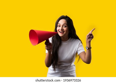 Indian young girl with megaphone made out of paper. Announcing, screeming or advertising while standing against yellow studio background - Shutterstock ID 1936973326