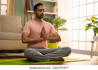 Indian young man doing namaste posture or yoga with closed eyes while sitting at home - concept of healthy lifestyle, fitness and self caring - Powered by Shutterstock