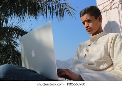 Indian Young Man With A Laptop On The Roof Under A Palm Tree. The Guy Works On The MacBook. India, Rishikesh, December 20, 2018.