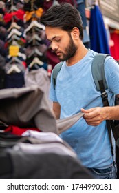 Indian Young Man Looking And Buying Clothing From Outdoor Street Market Of Delhi, India At Day Time.