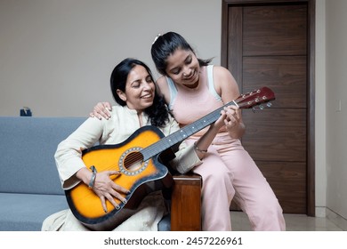 Indian Young Teenage Daughter Helping mother with Guitar Playing at home sitting on sofa, Mother Daughters Relation ship - Powered by Shutterstock