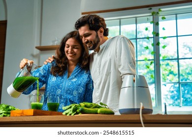 Indian young wife preparing fresh green spinach juice and serving it to her husband in kitchen, focusing on health and nutrition concept for a healthy lifestyle - Powered by Shutterstock