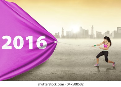 Indian young woman pulling a big banner with numbers 2016 while wearing sportswear, shot outdoors