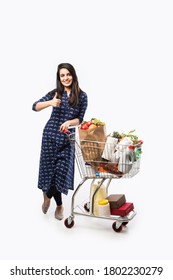 Indian young woman with shopping cart or trolly full of grocery, vegetables and fruits.  Isolated Full length photo over white background