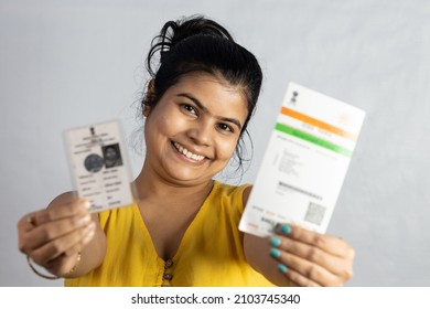 An Indian young woman smiling with ID card and voter card in hands on white background
