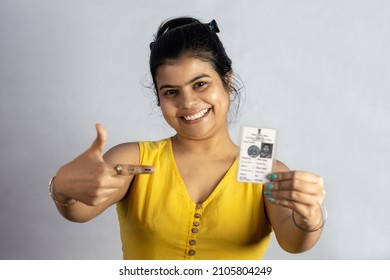 An Indian Young Woman Smiling And Pointing To Voter Card In Hand On White Background