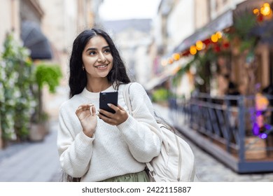 An Indian young woman walks the streets of the city, travels, uses the phone with a smile, searches through the navigator. - Powered by Shutterstock