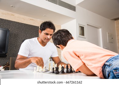 Indian/asian Father And Son Playing Chess At Home