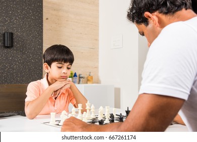 Indian/asian Father And Son Playing Chess At Home