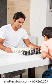 Indian/asian Father And Son Playing Chess At Home