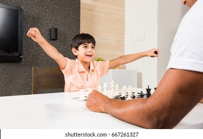 Indian/asian Father And Son Playing Chess At Home