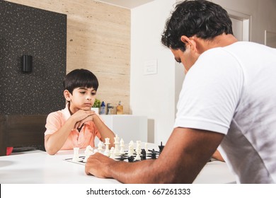 Indian/asian Father And Son Playing Chess At Home