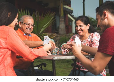 Indian/asian MODERN Family Playing Cards And Having Fun While Sitting In Lawn, Outdoor 