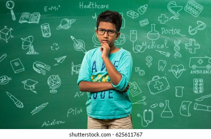 Indian/asian School Kid Or Boy In Spects In Thinking Pose, Standing Isolated Over Green Chalkboard Background With Education Doodles