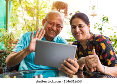 Indian/asian Senior Couple Video Chatting On Tablet/computer While Sitting At Couch Or In Garden At Home, Selective Focus
