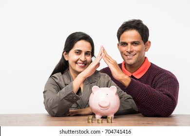 Indian/Asian Smart And Young Couple Saving Money In Piggy Bank For Buying A Dream Home Concept