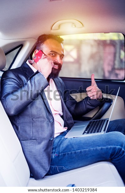 Indian/asian young businessman using\
laptop computer and phone inside the car, selective\
focus