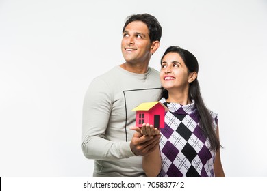 Indian/Asian Young Couple Buying / Dreaming For Home OR Real Estate Concept, Holding 3D Colourful Paper Model Of House. Isolated Over White Background
