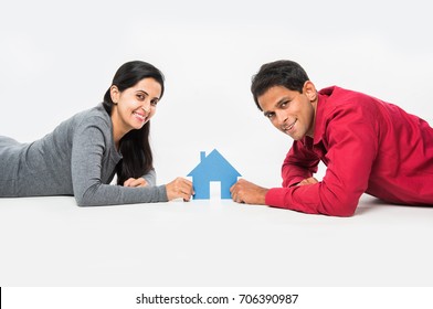 Indian/Asian Young Couple Buying / Dreaming For Home OR Real Estate Concept, Holding 3D Colourful Paper Model Of House. Isolated Over White Background
