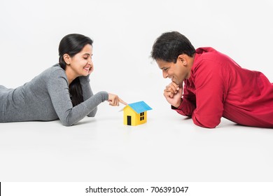 Indian/Asian Young Couple Buying / Dreaming For Home OR Real Estate Concept, Holding 3D Colourful Paper Model Of House. Isolated Over White Background
