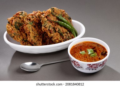 Indian's Most Popular Street Snack Called Palak Vada Or Spinach  Fritter In White Bowl  Souse Called Chana Rassa In Bowl And Green Chilli With Spoon On Gray Background 