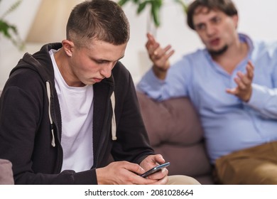 indifferent difficult teenager is sitting on couch with smartphone on Internet. father screams and threatens his son. Misunderstanding between father and son. Internet addiction and gadget addiction - Powered by Shutterstock