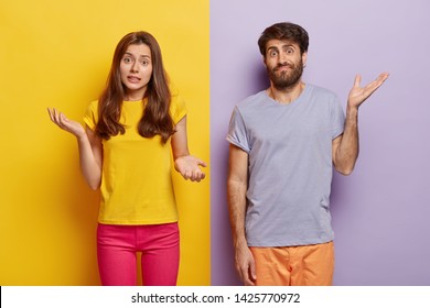 Indifferent Unbothered Woman And Man Spread Hands Sideways, Have No Idea, Dressed In Casual Outfit, Pose Against Different Color Background. Confused Questioned Couple With Clueless Expression Indoor