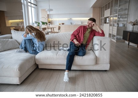 Indifferent uncaring man abuser with dissatisfied look sitting on sofa, neglecting wife, while offended upset desperate woman crying after quarrel, argue, disagreement. Family crisis, gaslighting