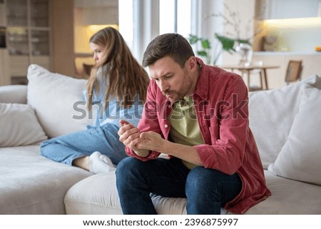 Indifferent uncaring man sitting on sofa, demonstratively examining hands, neglecting wife, and offended upset desperate woman after quarrel, argue, disagreement. Family crisis, conflict, gaslighting