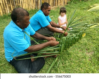 Indigenous Fijian Men Teach Young Tourist Girl How To Create A Basket From Weaving A Coconut Palm Leaves.Travel Fiji Concept, Real People. Copy Space