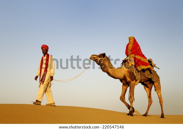 Indigenous Indian man and woman traveling through\
the desert riding\
camel.