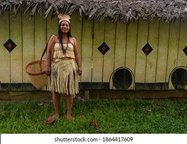 Indigenous woman from the Huitoto tribe of the Colombian Amazon in front of a maloka with a traditional basket