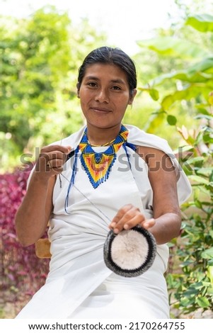 Indigenous woman from the Sierra Nevada de Santa Marta in traditional clothing weaving looking at the camera.