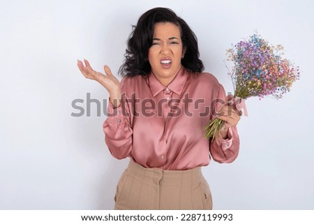 Indignant beautiful woman wearing knitted sweater over white background gestures in bewilderment, frowns face with dissatisfaction.