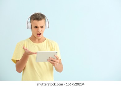 Indignant boy with tablet computer playing video games on light background - Powered by Shutterstock