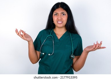 Indignant Doctor hispanic woman wearing surgeon uniform over white background gestures in bewilderment, frowns face with dissatisfaction.