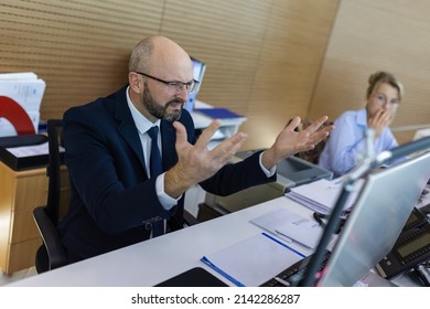 Indignant office worker sits at a desk in a modern office spaceappearing angry, annoyed and surprised.Surprised business partners at the workplace. In the center of attention is an indignant person.