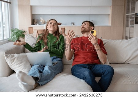Indignant, perplexed married couple gestures with hands hears noise loud sound from neighbors upstairs, disturbing them from working with laptop or relaxing at home. Perturbed man an woman looking up 