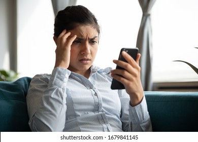 Indignant unhappy Indian young woman looking at smartphone screen, upset sad young girl worried by bad news reading in message, having problem with broken or discharged mobile device