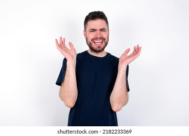 Indignant Young caucasian man wearing black T-shirt over white background gestures in bewilderment, frowns face with dissatisfaction.