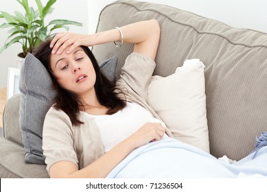 Indisposed woman feeling her temperature while resting on the sofa at home - Powered by Shutterstock