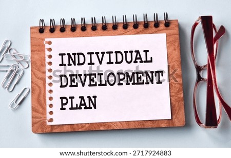 INDIVIDUAL DEVELOPMENT PLAN - words on a white sheet of paper on the background of a notebook, glasses and paper clips