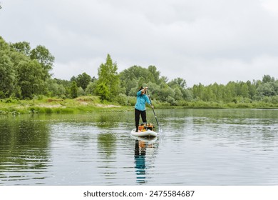 An individual engages in paddleboarding on a tranquil lake, surrounded by lush green forest. The calm waters and beautiful natural surroundings make for a peaceful outdoor activity. - Powered by Shutterstock