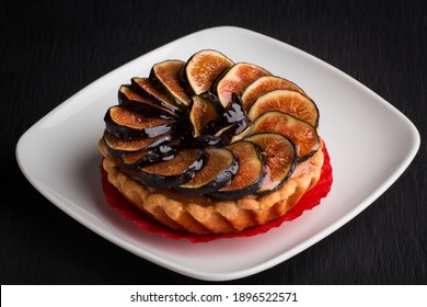 Individual Fig Tart With Cookie Crust Base On An Elegant White Plate Served As A Dessert At A Fancy Restaurant For Dinner With A Black Wooden Board As Background