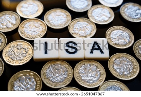 Individual Saving Account. Macro view of ISA cubes amid scattered pound coins forming money pattern highlighting UK tax free savings.