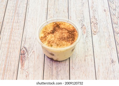 Individual tiramisu dessert with cinnamon and powdered chocolate inside a home delivery container on wooden table