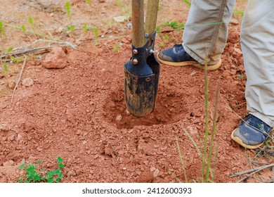 An individual using hand post hole digger to dig fence post